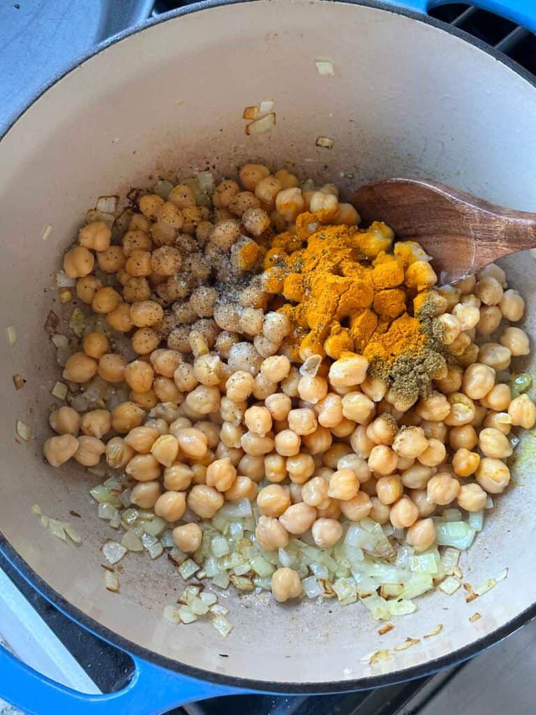 Adding turmeric and cumin to onions and chickpeas in a pot.