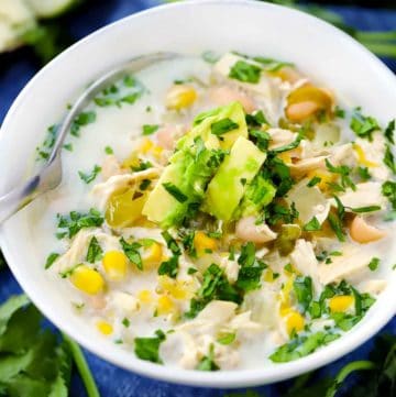 A white bowl filled with white chicken chili topped with avocado and cilantro.