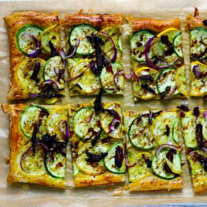 Square photo of a zucchini and summer squash puff pastry tart cut into pieces.